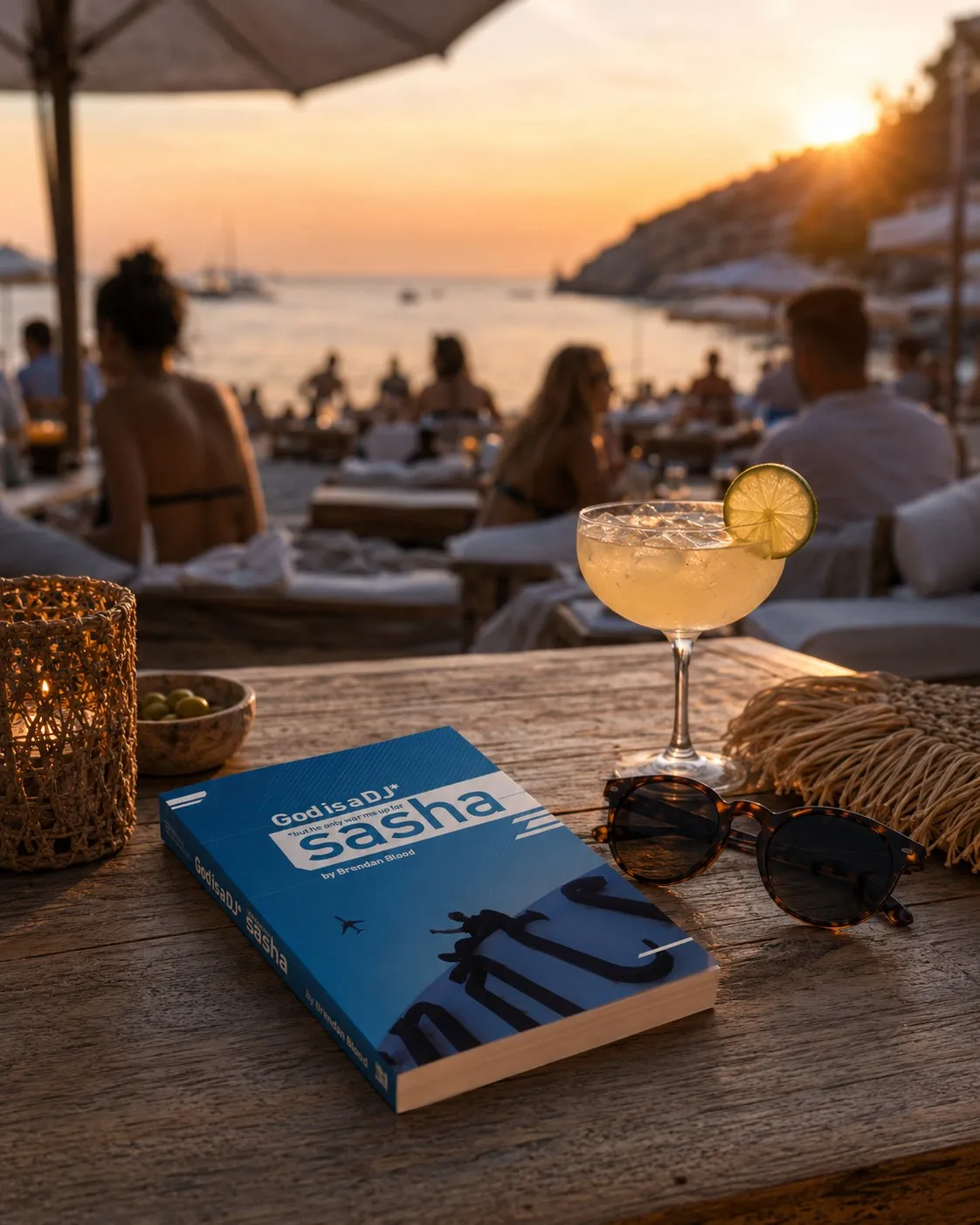 The paperback of God is a DJ* on a wooden table at a beach club at sunset.